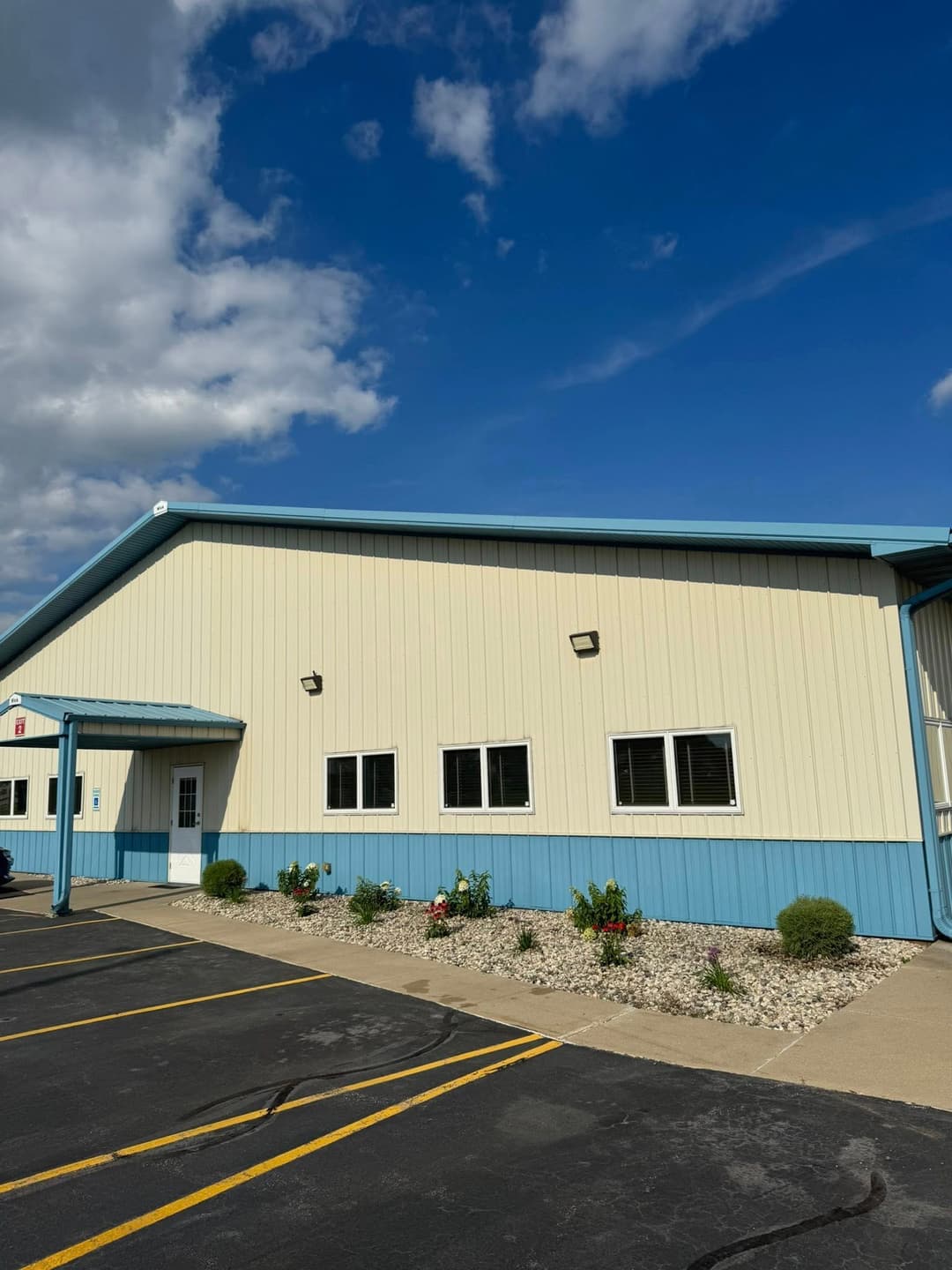 Steel building exterior with blue trim and landscaped garden under a cloudy sky.